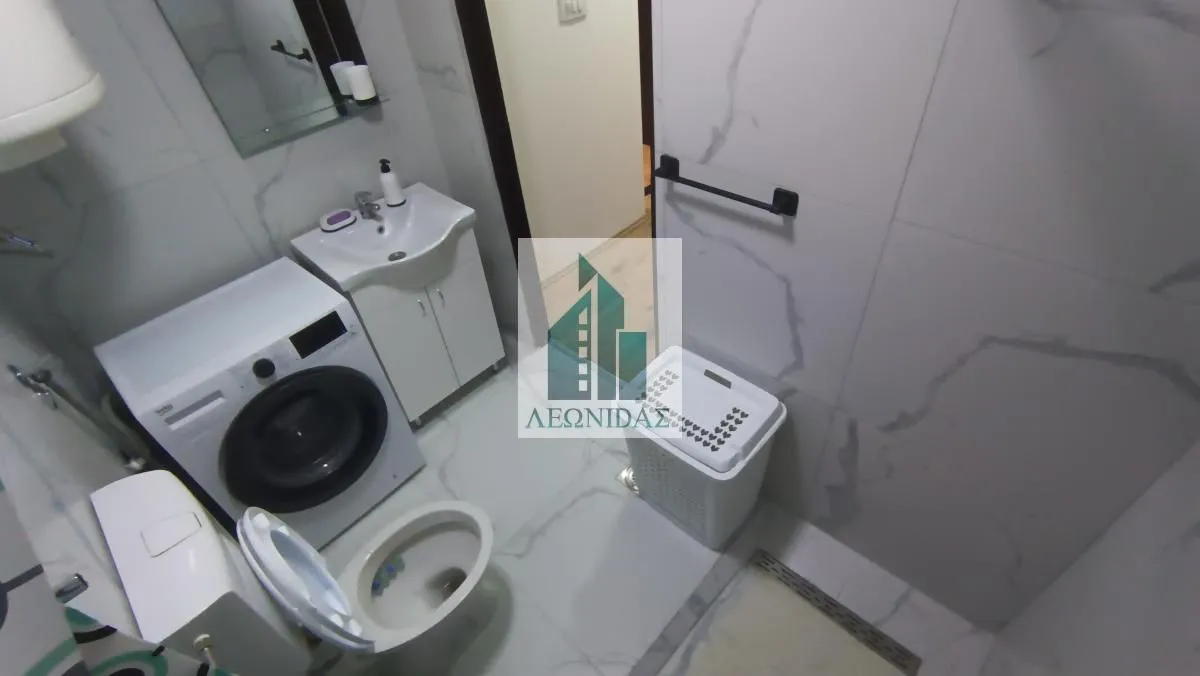 Compact bathroom with a shower cabin, washbasin, and washing machine.