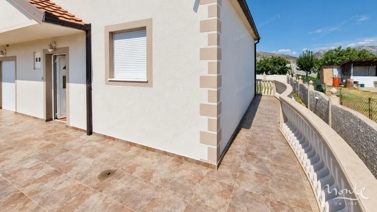 Pogled na popločano dvorište i fasadu kuće sa ulaznim vratima.
