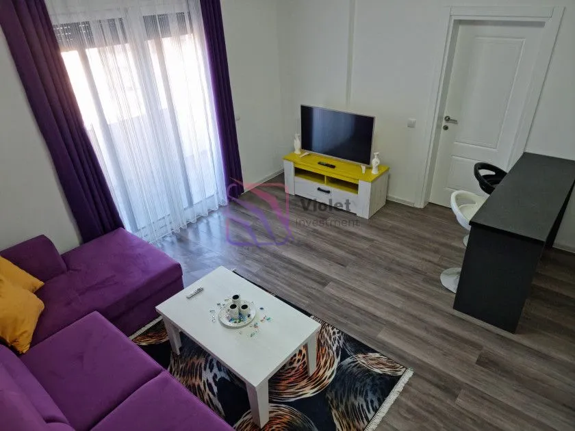 Dnevna soba sa ljubičastom garniturom, TV komodom i malim stolom.