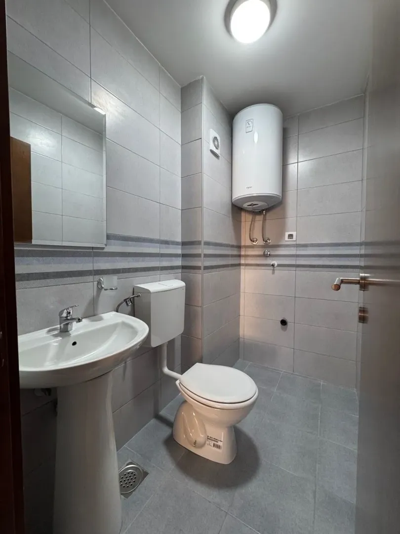 Moderno opremljeno kupatilo sa svijetlim pločicama, umivaonikom i wc šoljom.