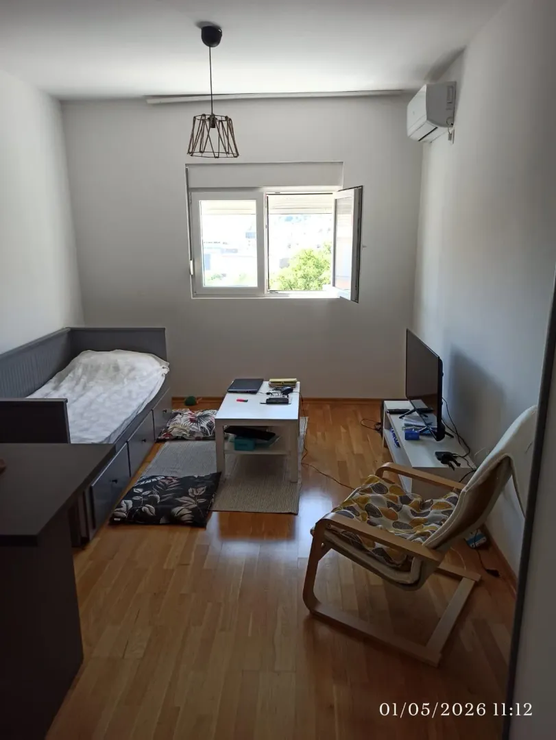 Manja spavaća soba sa krevetom, foteljom, TV-om i radnim stolom.