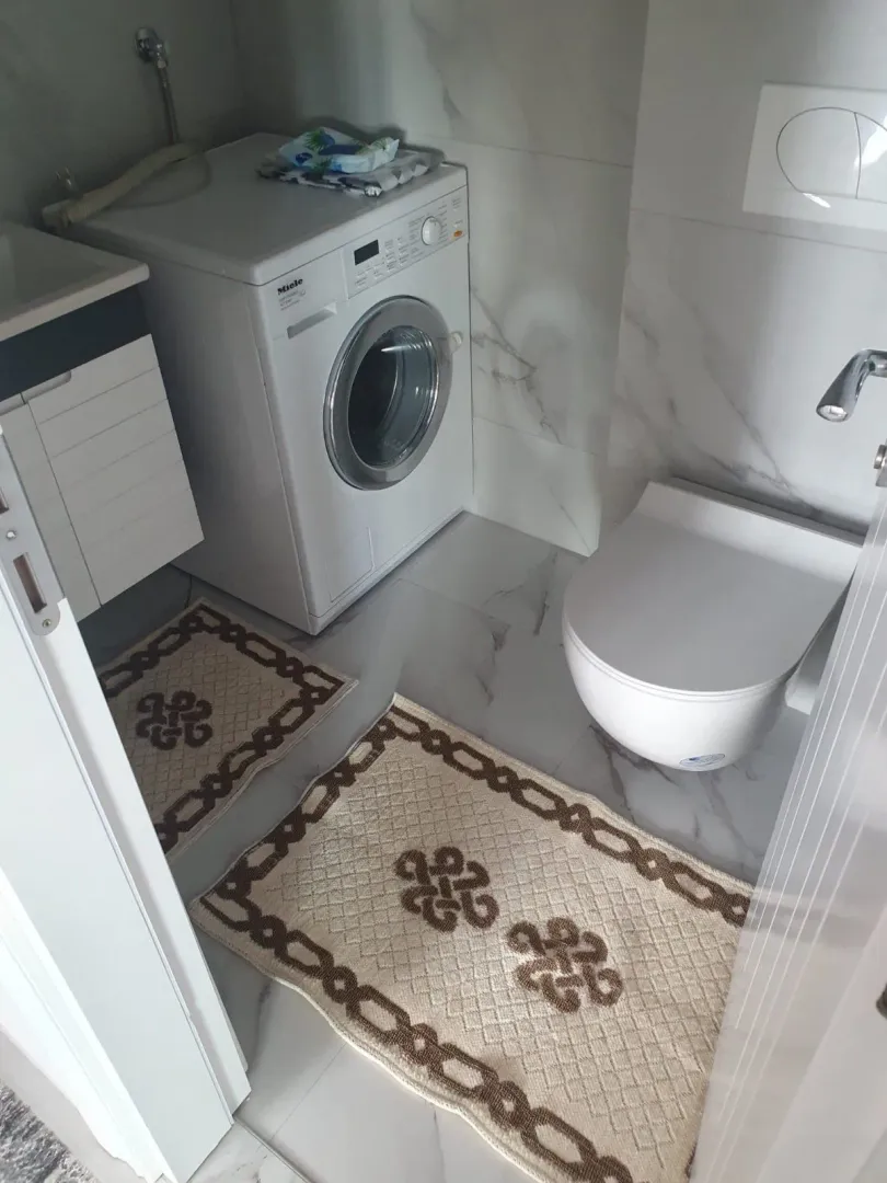Manje kupatilo sa WC šoljom, veš mašinom i umivaonikom.