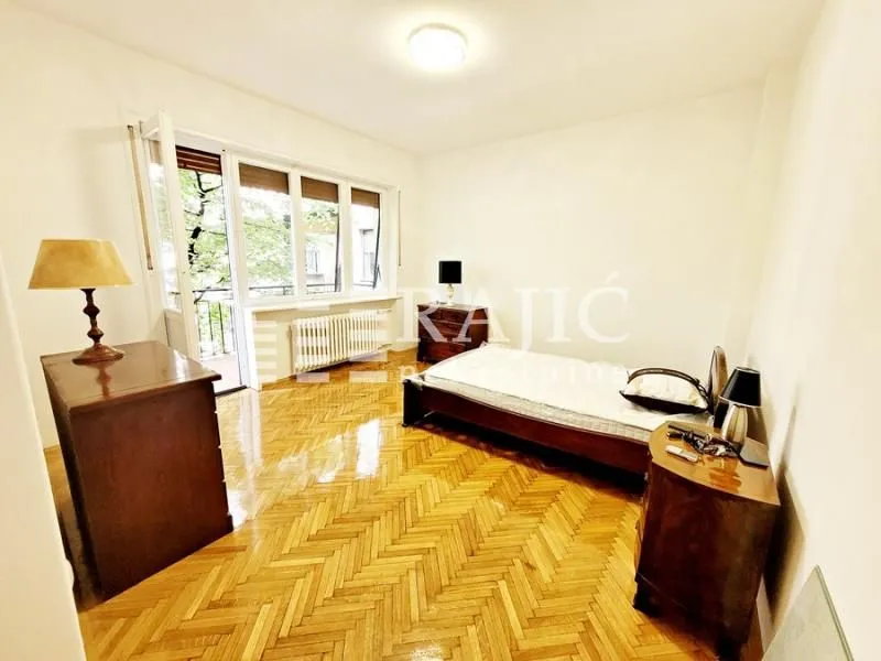 Furnished bedroom with a bed and wooden parquet flooring.