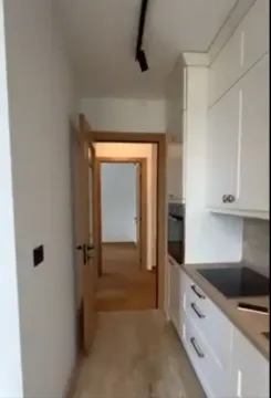 Uski kuhinjski prostor sa bijelim elementima koji vodi ka hodniku. - image 4