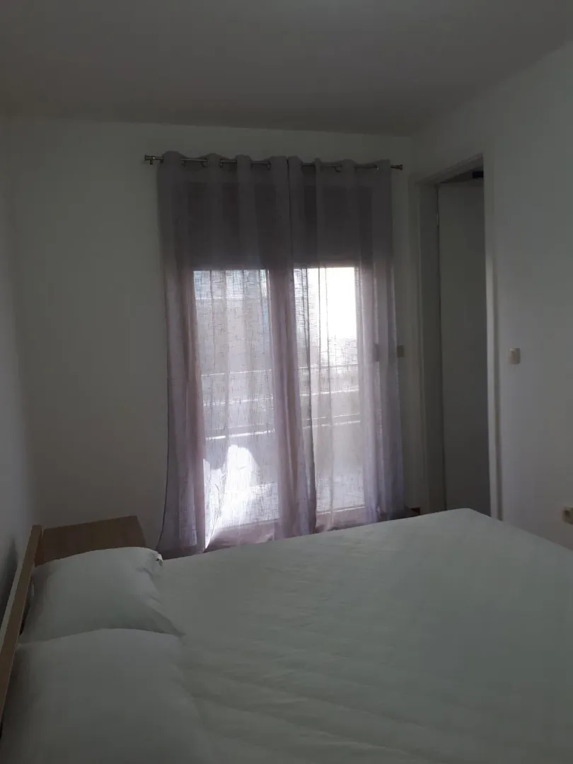 Spavaća soba sa bračnim krevetom i prozorom sa zavjesama.