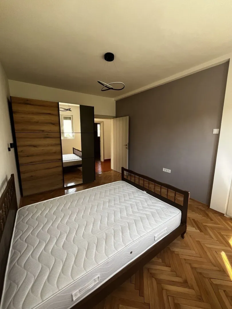 Svijetla spavaća soba sa drvenim krevetom i velikim ormarom sa ogledalom.