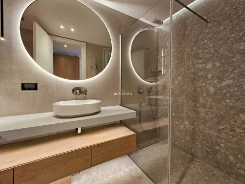 Modern bathroom with a sink, large round illuminated mirror, and a walk-in shower. - image 6