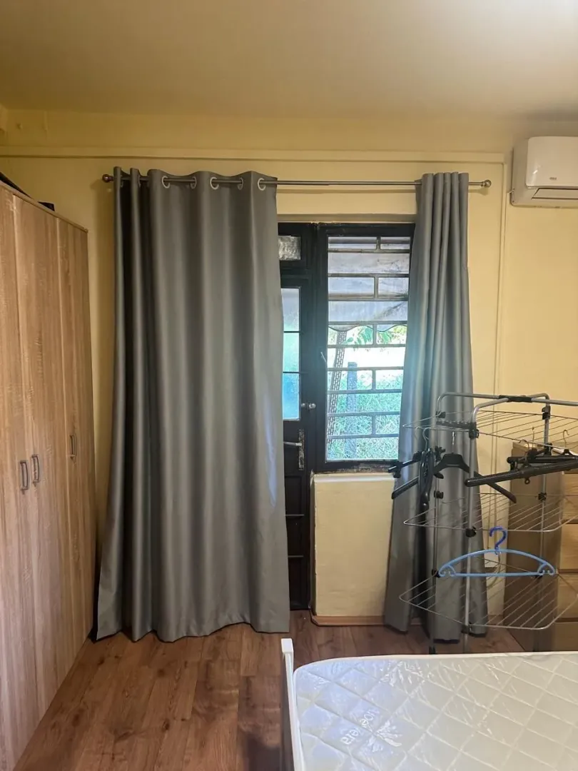 Manja spavaća soba sa krevetom, ormarom i prozorom sa zavjesama.