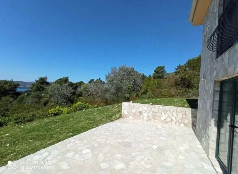 Popločano dvorište ispred kamene kuće sa pogledom na zeleno okruženje.