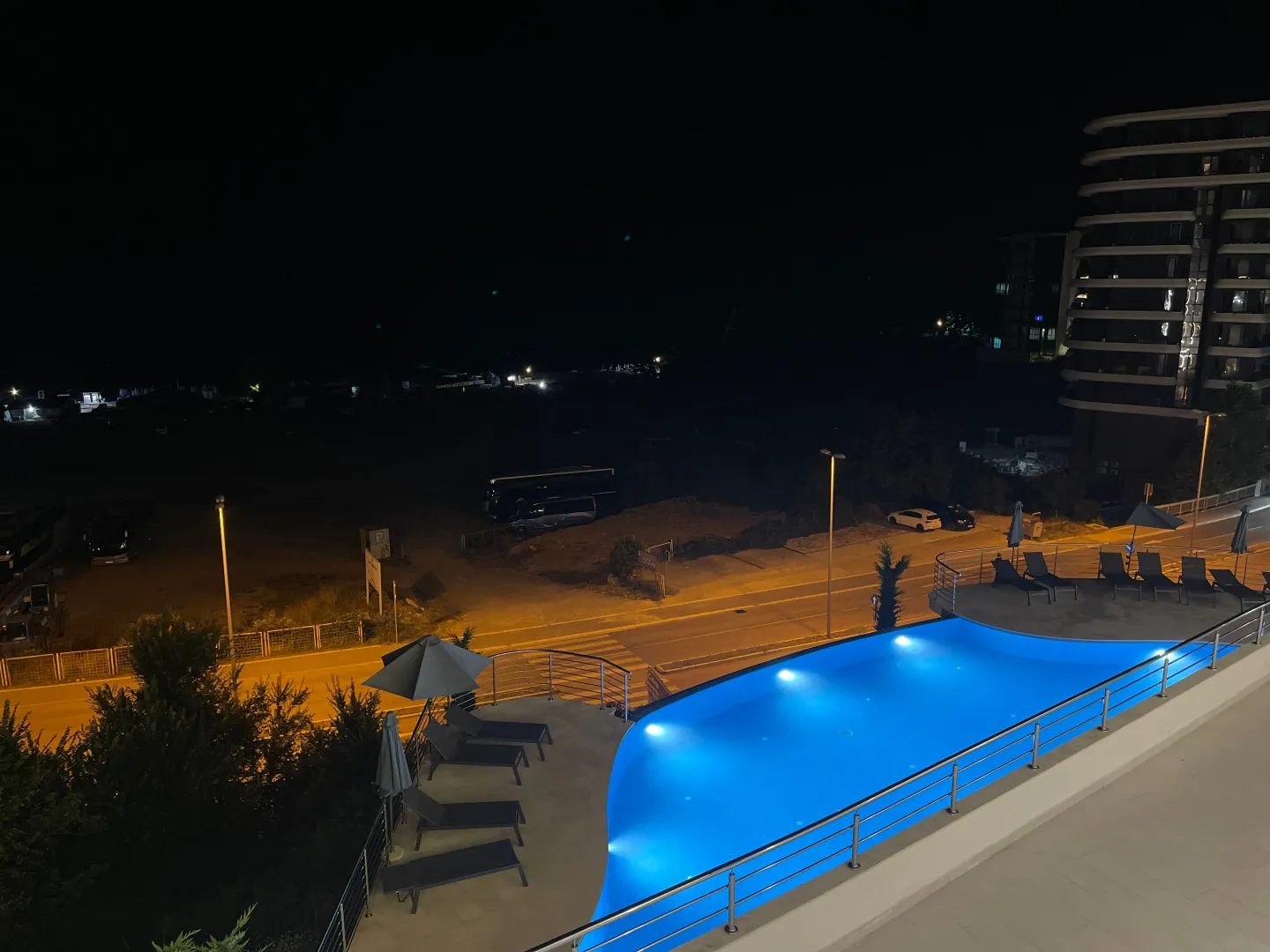 Noćni pogled na spoljašnjost zgrade sa osvijetljenim bazenom i ležaljkama.