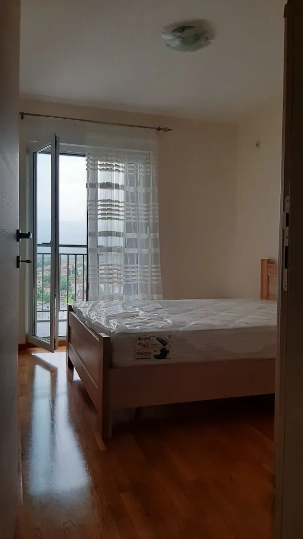 Svijetla spavaća soba sa drvenim krevetom i izlazom na balkon.