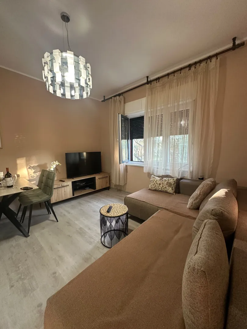 Udobna dnevna soba sa ugaonom garniturom, trpezarijskim delom i modernim lusterom.