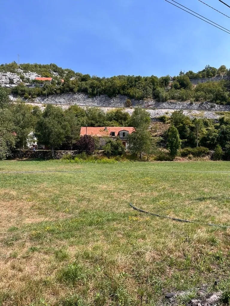 Pogled na kuću sa velikim travnjakom i brdima u pozadini.