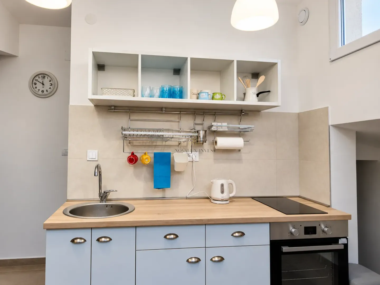 Compact kitchen with sink, built-in cooktop and upper cabinets.