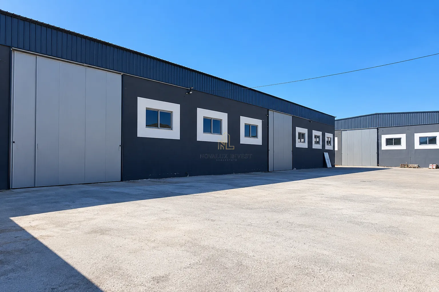View of the exterior of a commercial building with large doors and a concrete patio.
