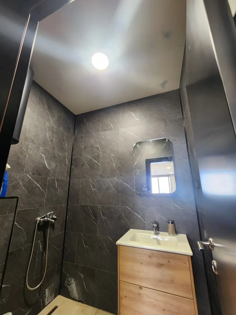 Small bathroom lined with dark tiles featuring a sink and mirror.