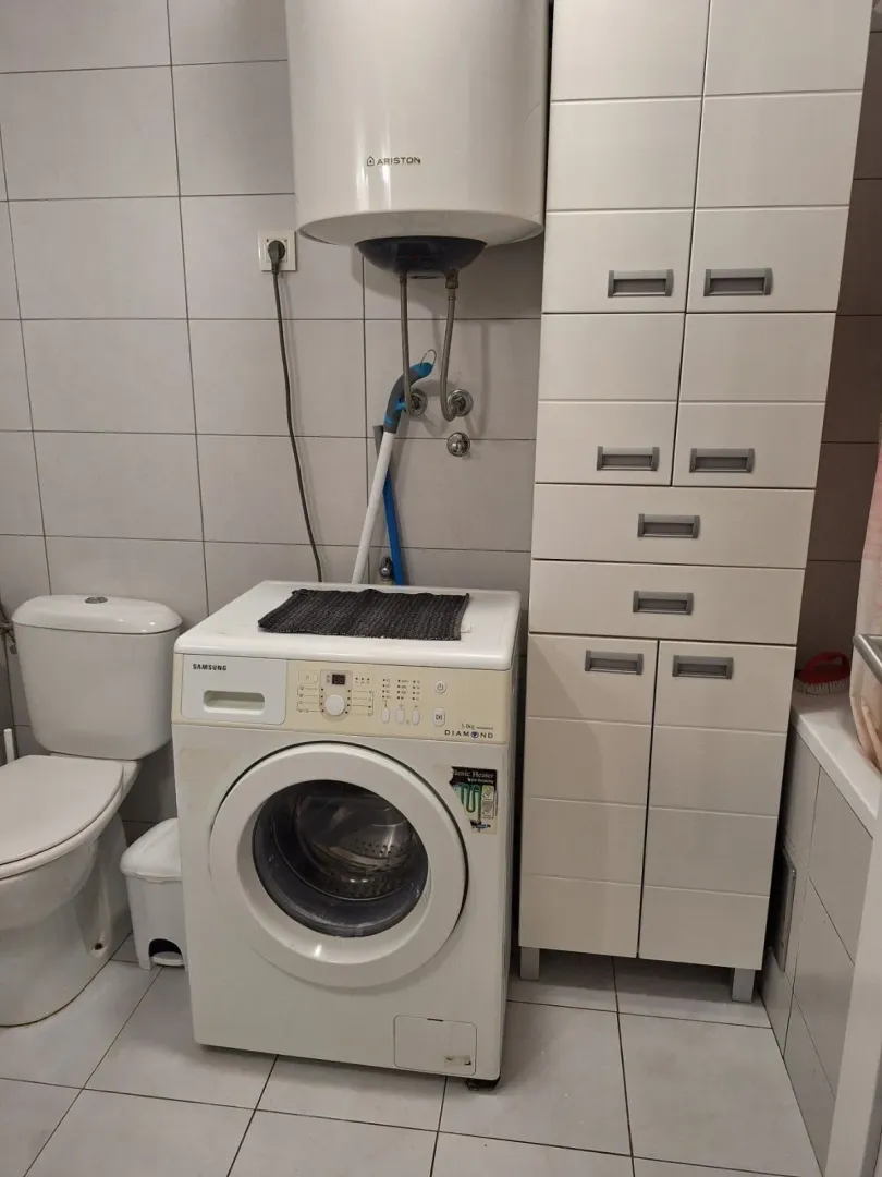 Manje kupatilo opremljeno sanitarijama, mašinom za veš i ormarićem.