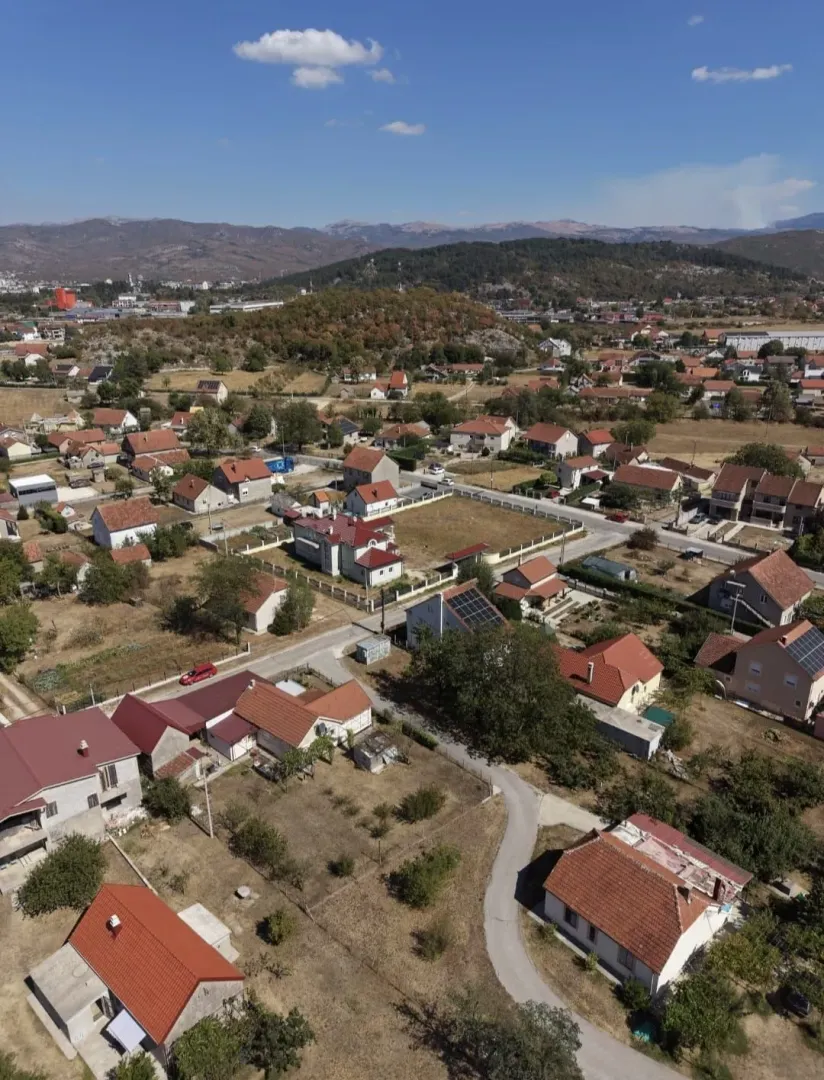 Pogled iz vazduha na naselje sa porodičnim kućama i okolnim zelenilom.