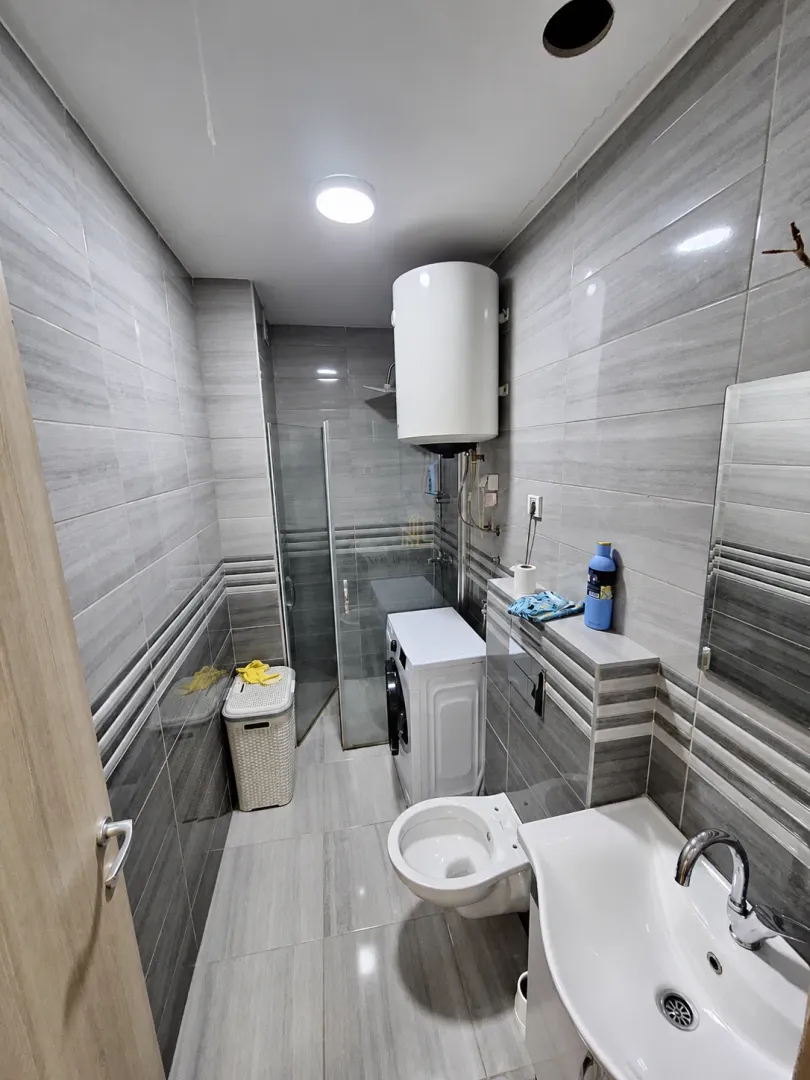 Kupatilo opremljeno sivim pločicama, sanitarijama, tuš kabinom i veš mašinom.