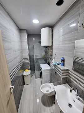 Kupatilo opremljeno sivim pločicama, sanitarijama, tuš kabinom i veš mašinom. - image 7