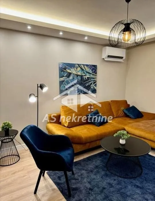 Dnevna soba sa ugaonom garniturom, foteljom i modernim osvetljenjem.