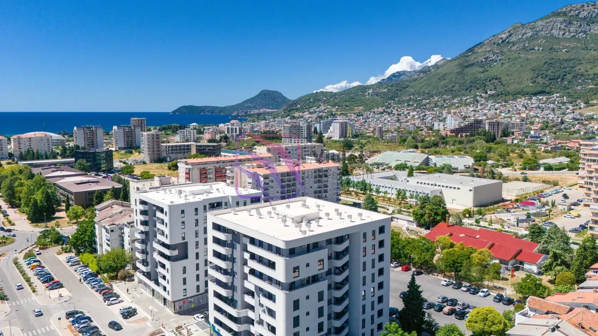 Pogled iz vazduha na grad sa zgradama, planinama i morem u pozadini.