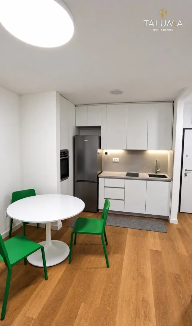 Modern kitchen with white cabinetry, built-in appliances, and a dining table with green chairs.