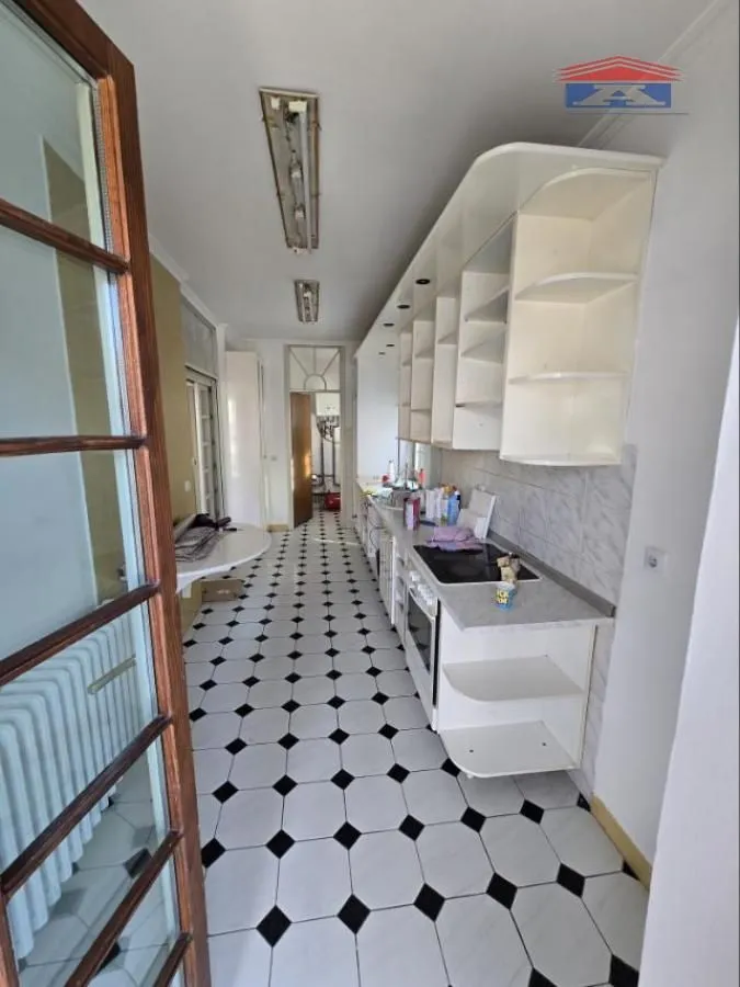 Long kitchen with white cabinetry and black and white ceramic floor tiles.