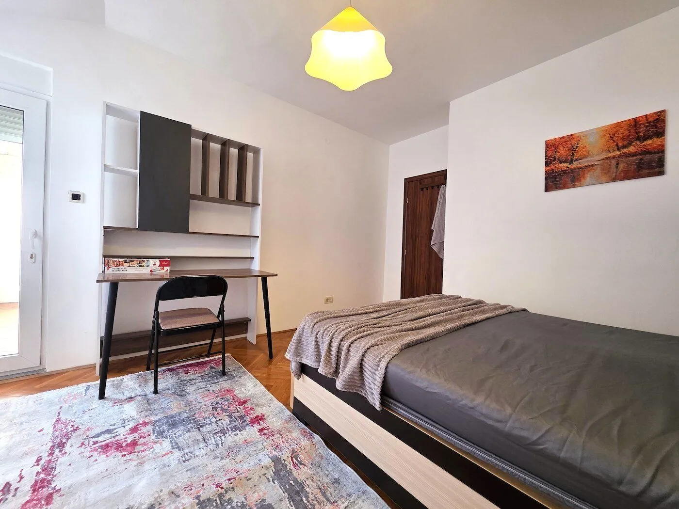 Furnished bedroom with a bed, desk, and rug.