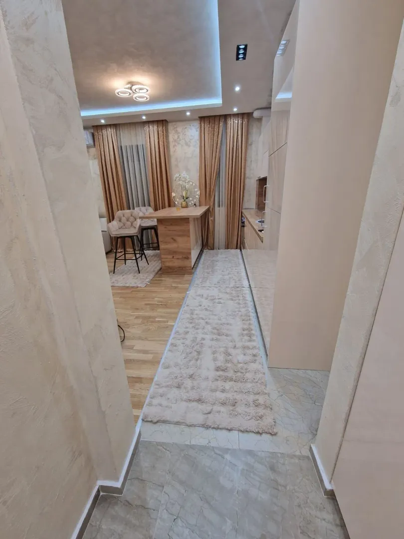 A bright kitchen with a dining table and bar stools viewed from the hallway.