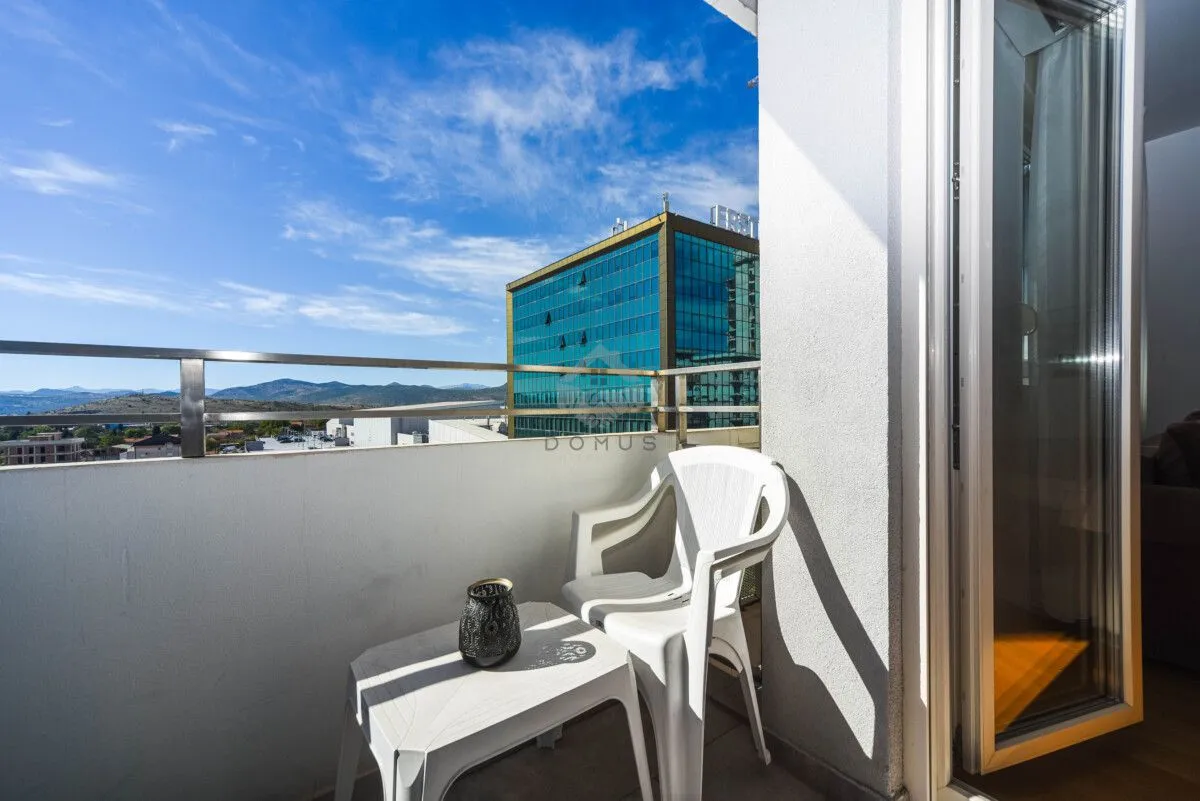 Balkon sa bijelim plastičnim stolom, stolicom i pogledom na grad.