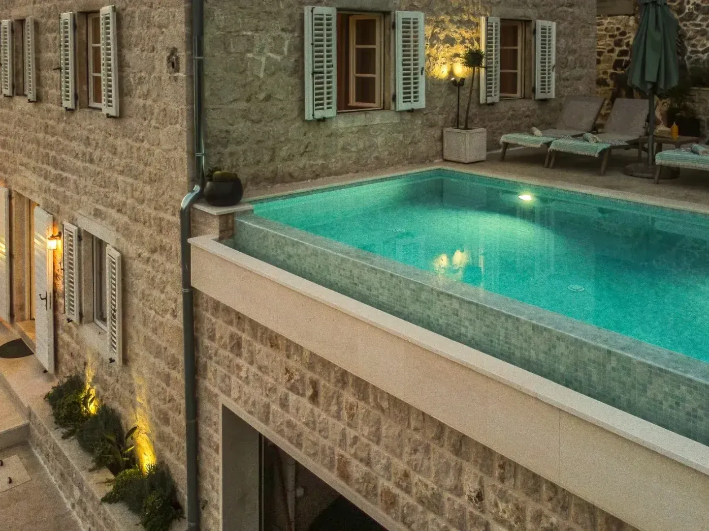 Swimming pool with a terrace in front of a stone house.