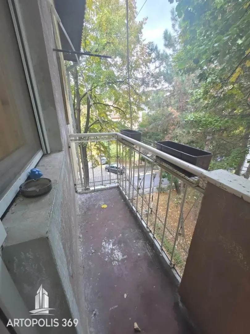 Small narrow balcony with metal railing and view of greenery and street.