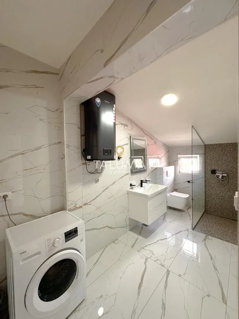 Modern bathroom with a walk-in shower, washbasin, and washing machine.
