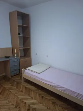 A bright bedroom with a single bed, a study desk, and a wooden shelving unit. - image 13