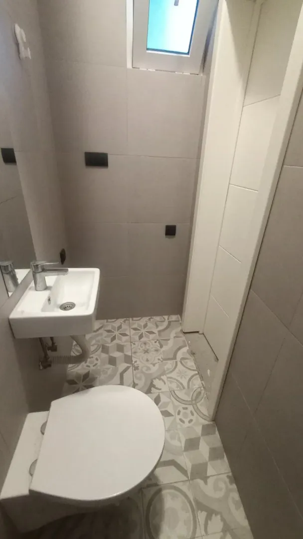 Manje kupatilo sa umivaonikom, šoljom i pločicama sa dezenom.