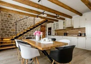 Modern kitchen with a dining area, exposed stone wall, and wooden ceiling beams.