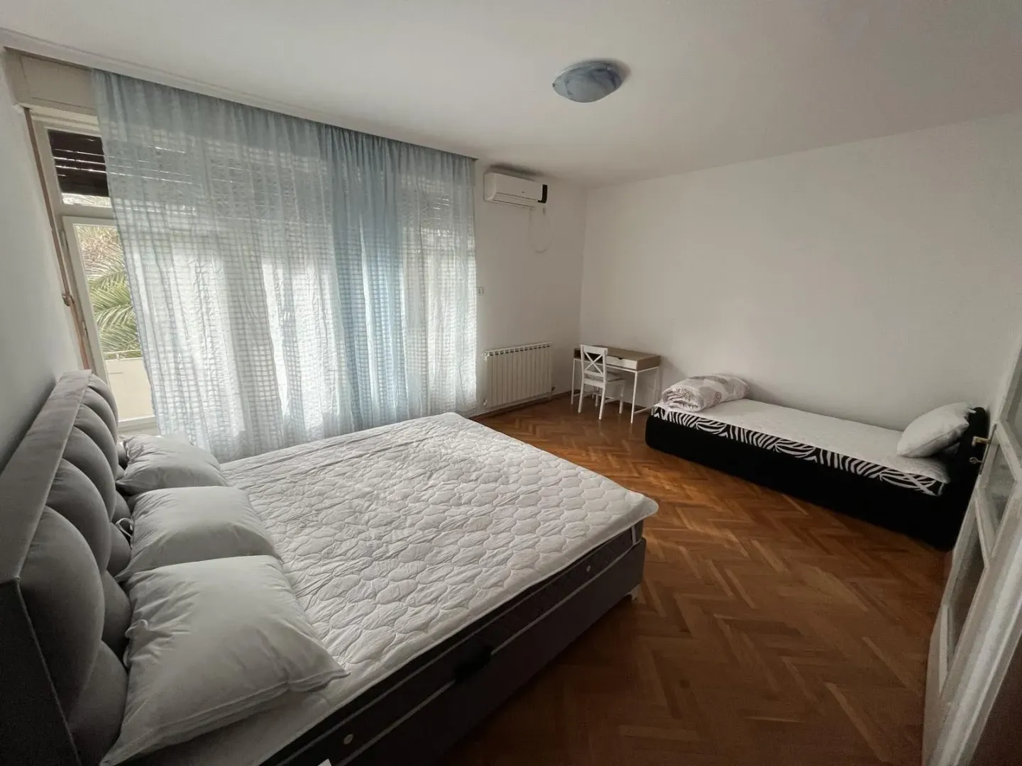 Svijetla spavaća soba sa dva kreveta i radnim stolom.