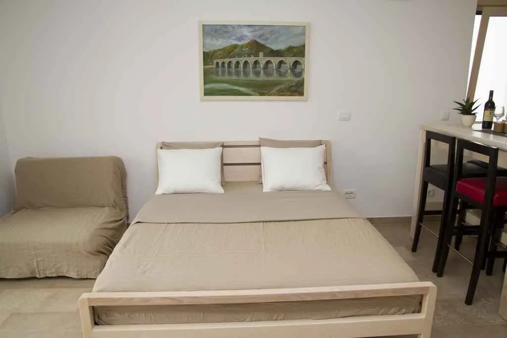 Svijetla spavaća soba sa bračnim krevetom, pomoćnim ležajem i šankom.