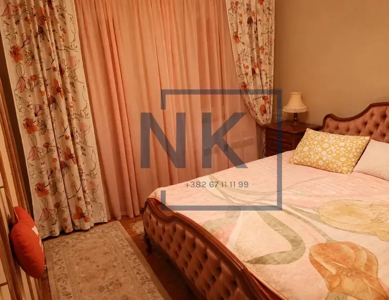 Furnished bedroom with a double bed, bedside table, and a window with curtains.