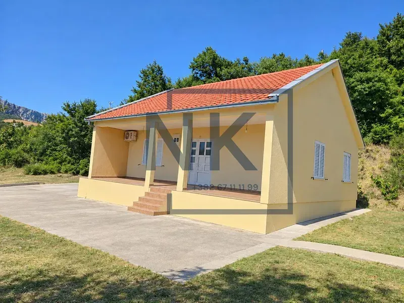 Pogled na spoljašnjost kuće sa natkrivenom terasom i popločanim dvorištem.