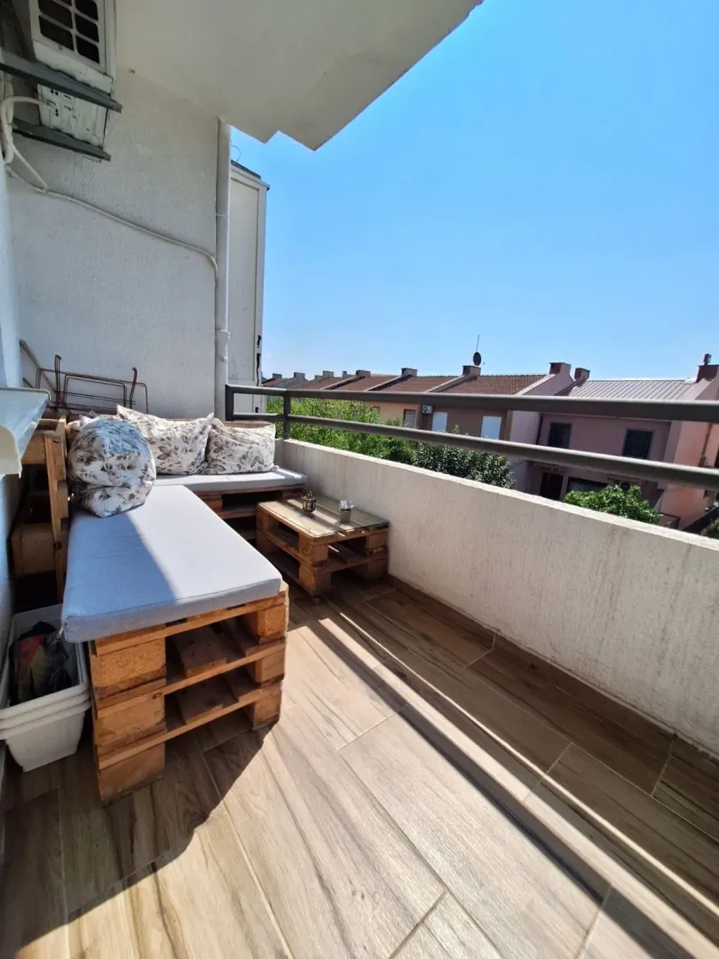 Manji namješten balkon sa garniturom od paleta i pogledom na okolne zgrade.