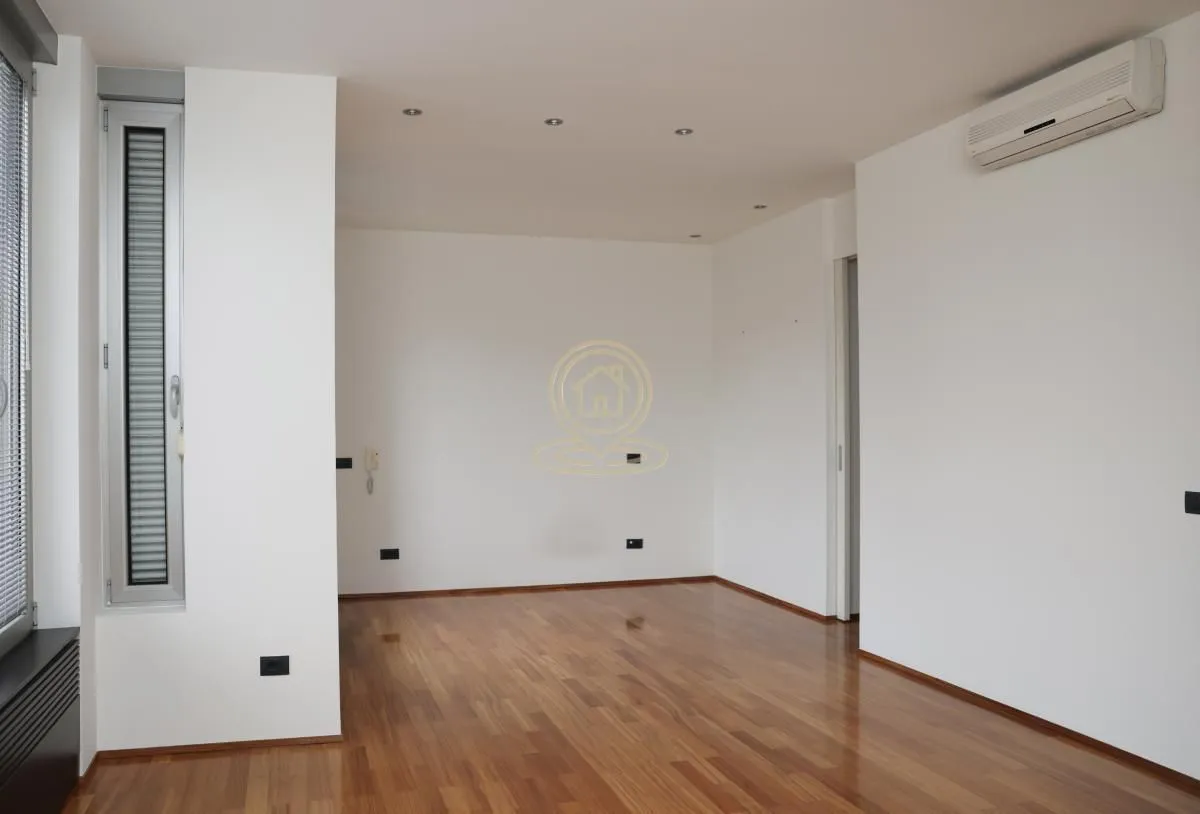 Empty room with white walls, wooden parquet flooring, and an air conditioning unit.