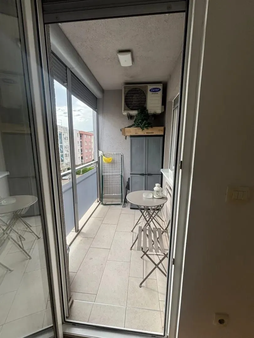 Manji zatvoreni balkon sa stolom, stolicama i klima uređajem.