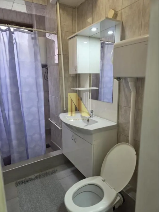 Kupatilo sa umivaonikom, ogledalom, WC šoljom i tuš kabinom sa zavesom.
