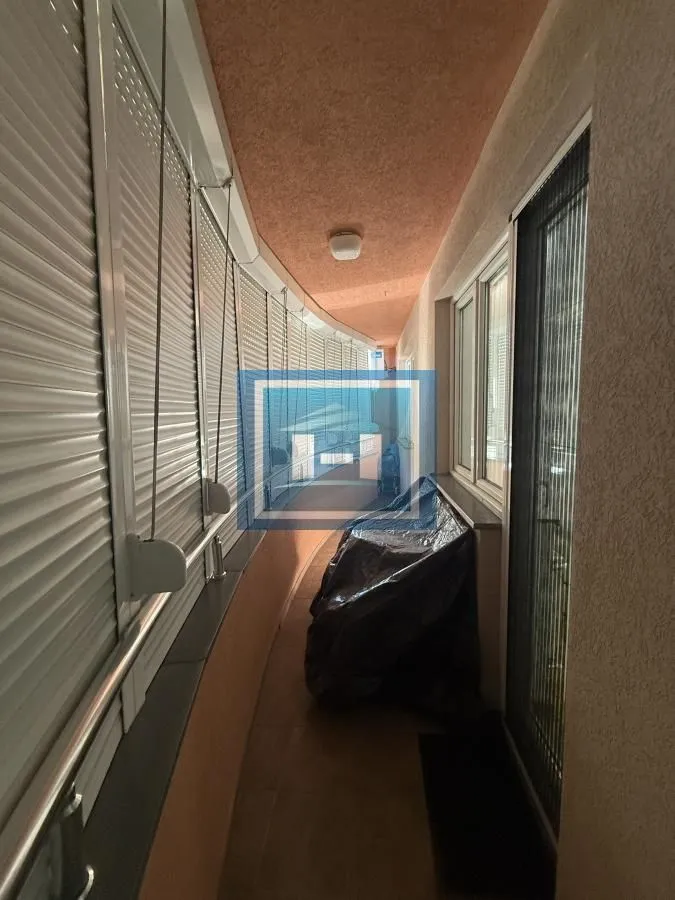 Dugačak zastakljeni balkon sa roletnama na prozorima.