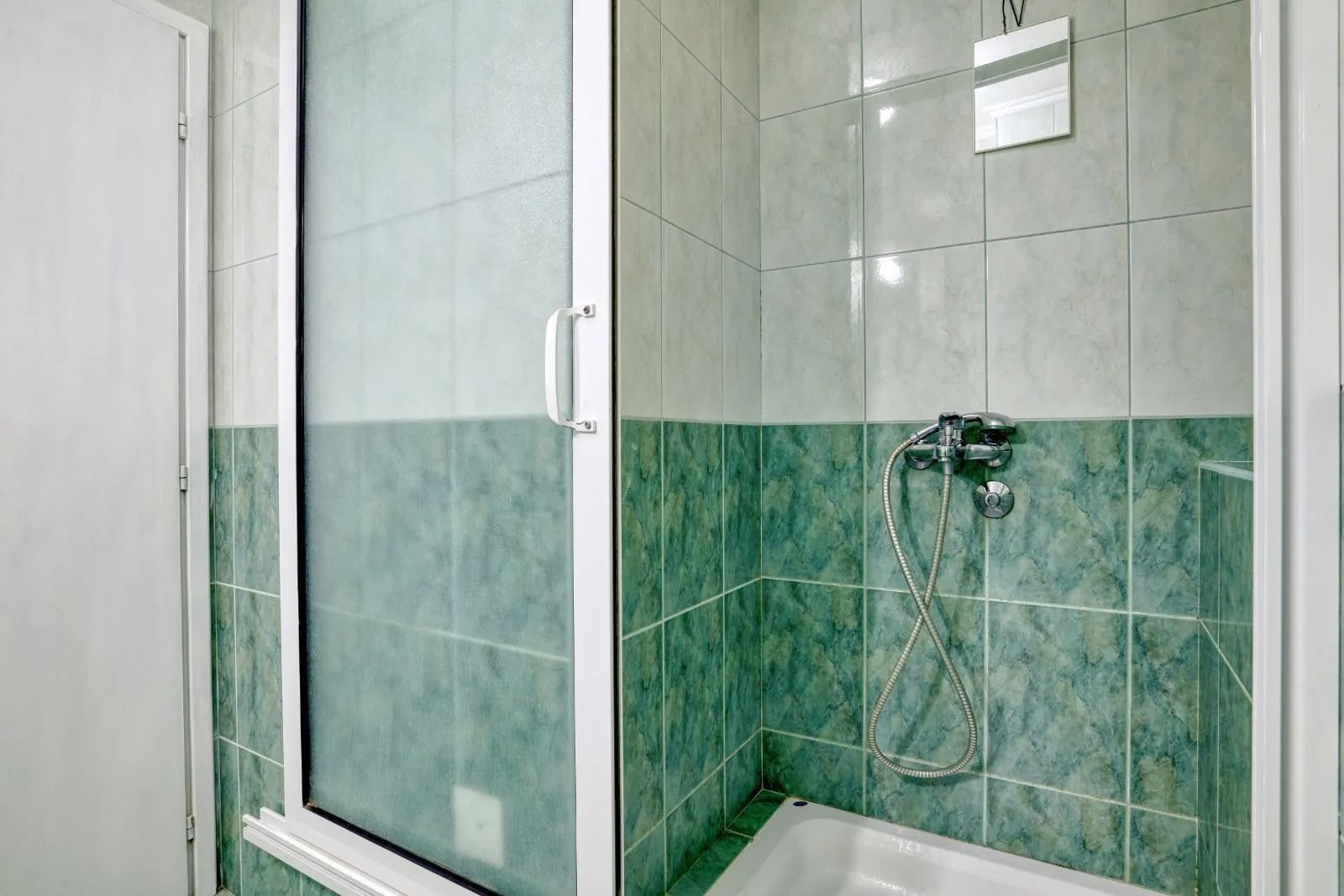 A shower cabin with glass doors and green tiles in the bathroom.