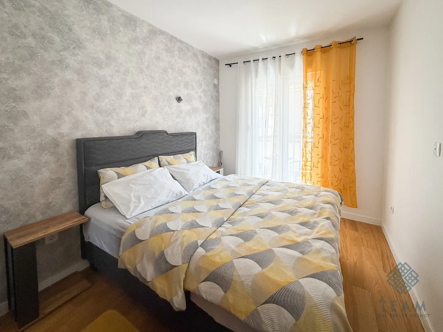 Furnished bedroom with a double bed and a window with yellow curtains.