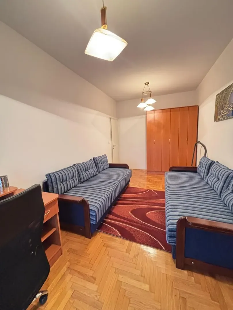 Dnevna soba sa dva plava kauča, tepihom i drvenim ormarom.