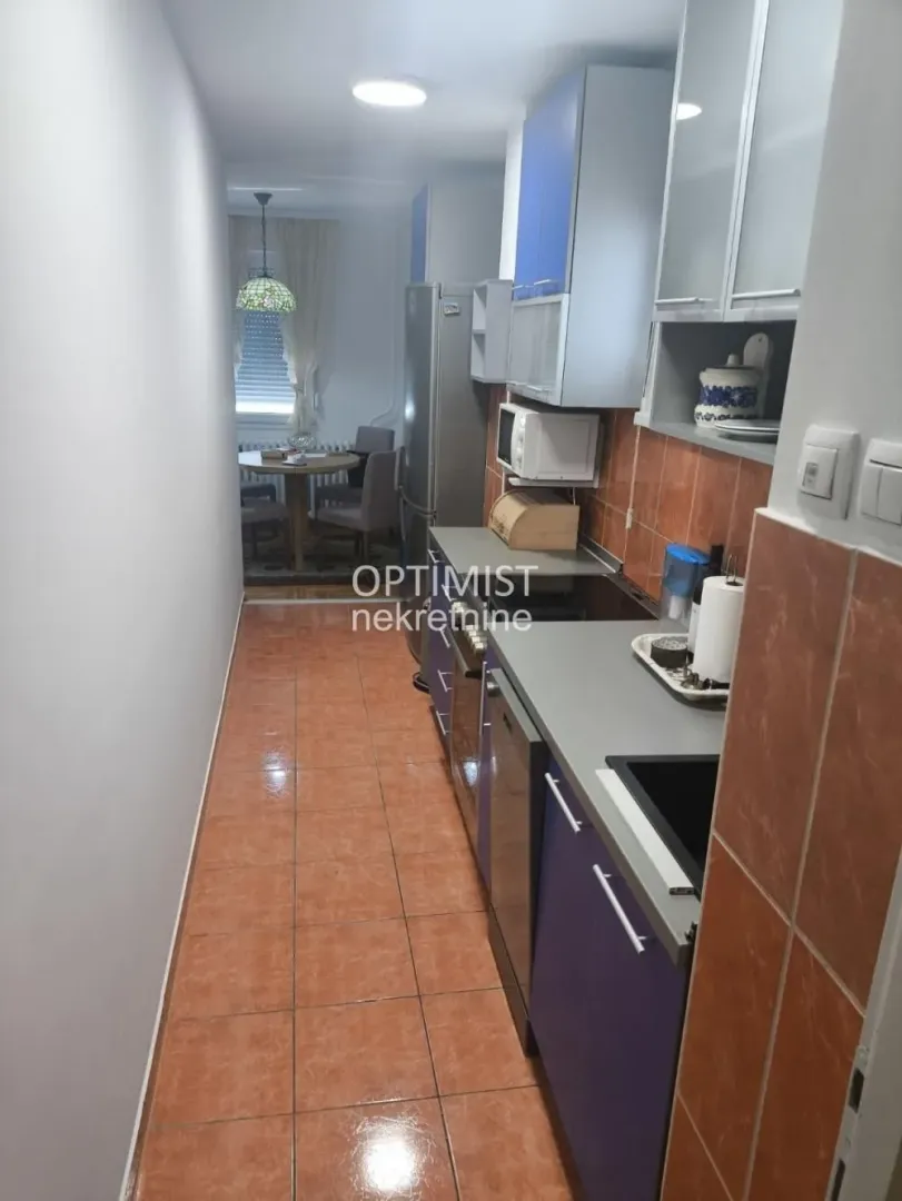 Narrow kitchen with cabinets and a dining area in the background.